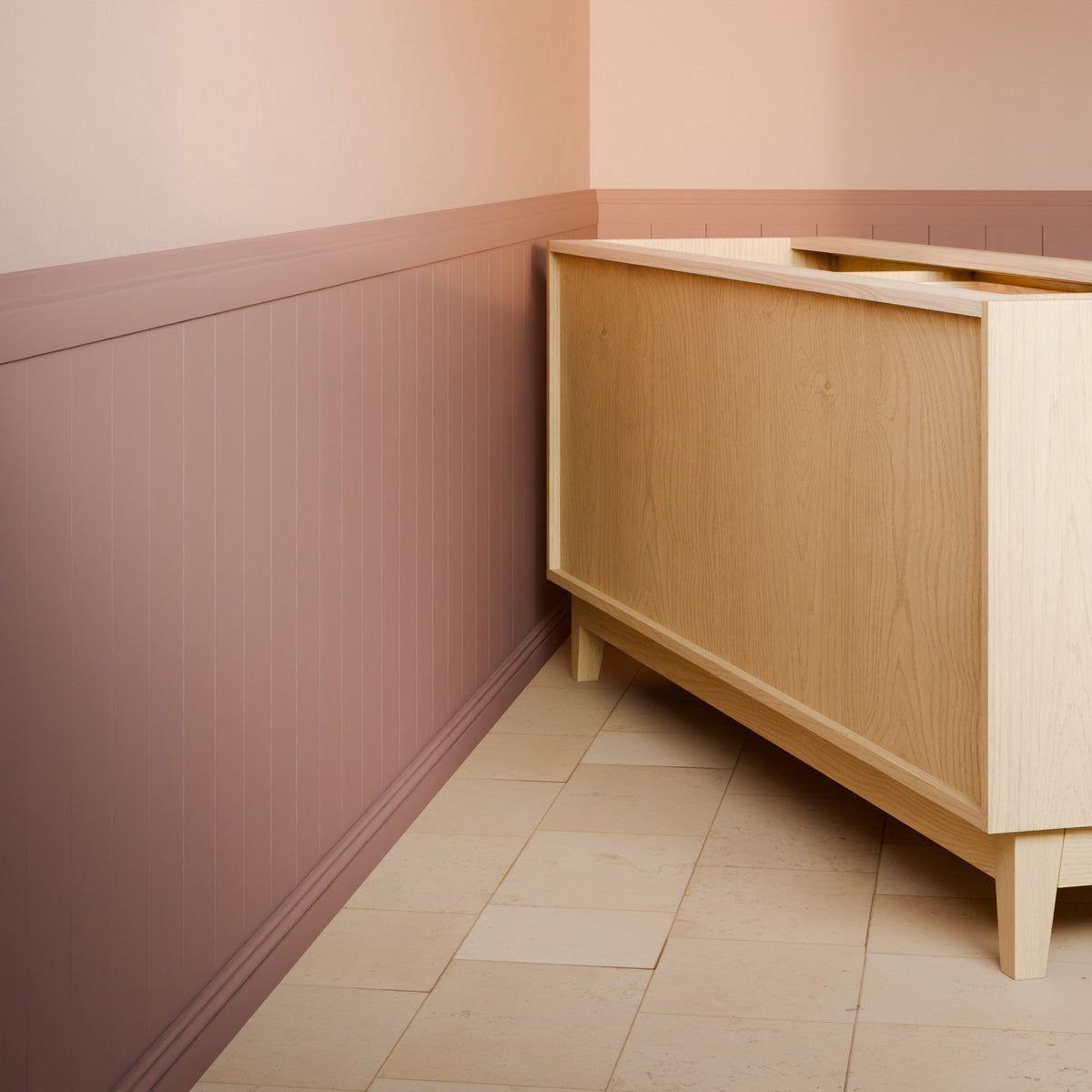 A light natural wood sideboard cabinet shown in a styled interior corner with a dusty rose wainscoted wall, pale pink upper wall, and beige tile floor.