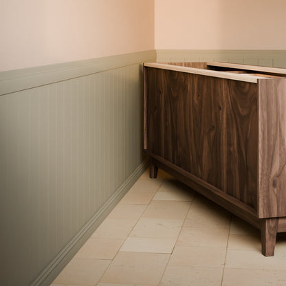 A dark wood cabinet or sideboard shown in a real interior corner with beige tile flooring, pale walls, and wainscoting.