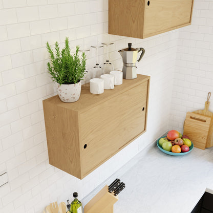 The Krovel Hardwood Cupboard Shelf is wall-mounted and displays a potted plant, four mugs, upside-down wine glasses, and a moka pot. Beneath it, a white countertop holds a fruit bowl, cutting boards, and utensils by white tiles.