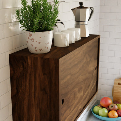 The Krovel Hardwood Cupboard Shelf stands against a white tiled wall, topped with a potted plant, three white mugs, and a silver stovetop espresso maker. Nearby on the counter is a bowl of fruit.
