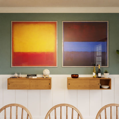 Two abstract paintings hang above the Krovel Floating Storage Cabinet in Cherry, which displays decor, books, wine, and glasses. The left painting is yellow and red; the right features blue and brown. Light wooden chairs sit in front.