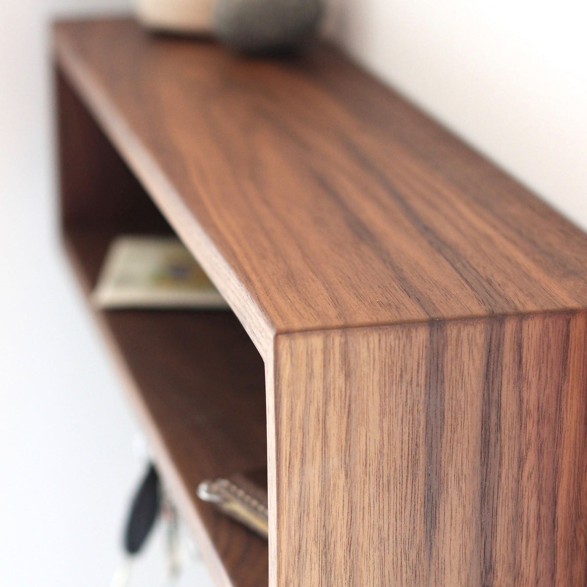 Close-up of the Krovel Entryway Organizer in Walnut—a minimalist, rectangular floating shelf with a smooth finish, neatly holding a set of keys and a folded bill on the lower tier.