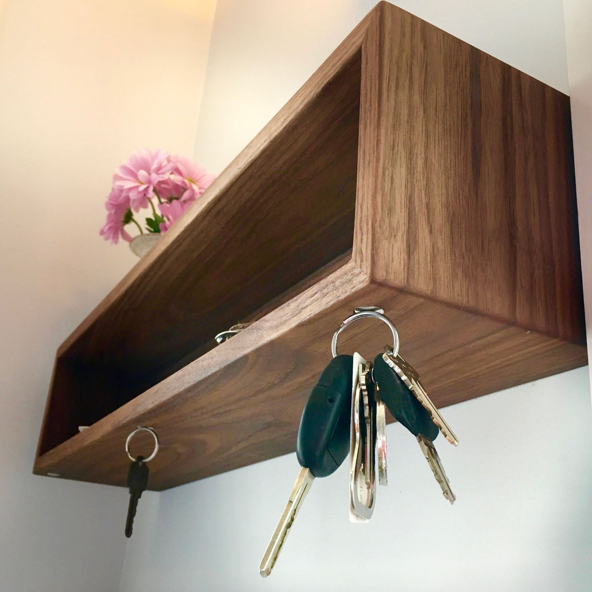 The Krovel Entryway Organizer in Walnut is a handmade floating shelf with magnetic hooks for keys and a petite pink floral accent, ideal for organizing your home's entryway.
