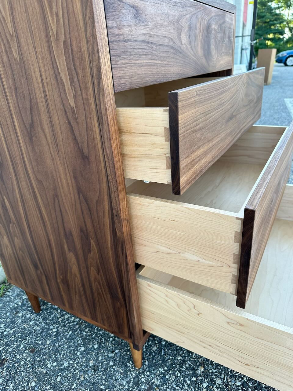 A close-up of the Krovel Furniture Co. 4 Drawer Dresser in Walnut - SAMPLE outdoors, with two drawers partially open to highlight the striking contrast of light and dark wood tones, solid hardwood construction, and finely crafted dovetail joints.