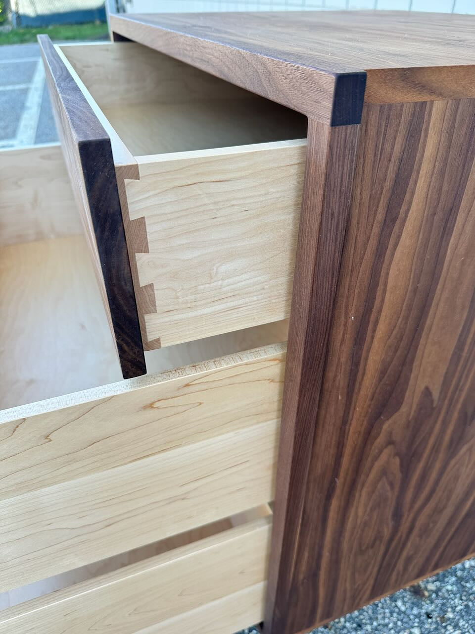 A close-up of the 3 Drawer Dresser in Walnut - SECOND by Krovel Furniture Co. shows an open drawer, highlighting dovetail joints that connect the light solid hardwood interior to the darker walnut-finished exterior, all treated with a zero-VOC finish.