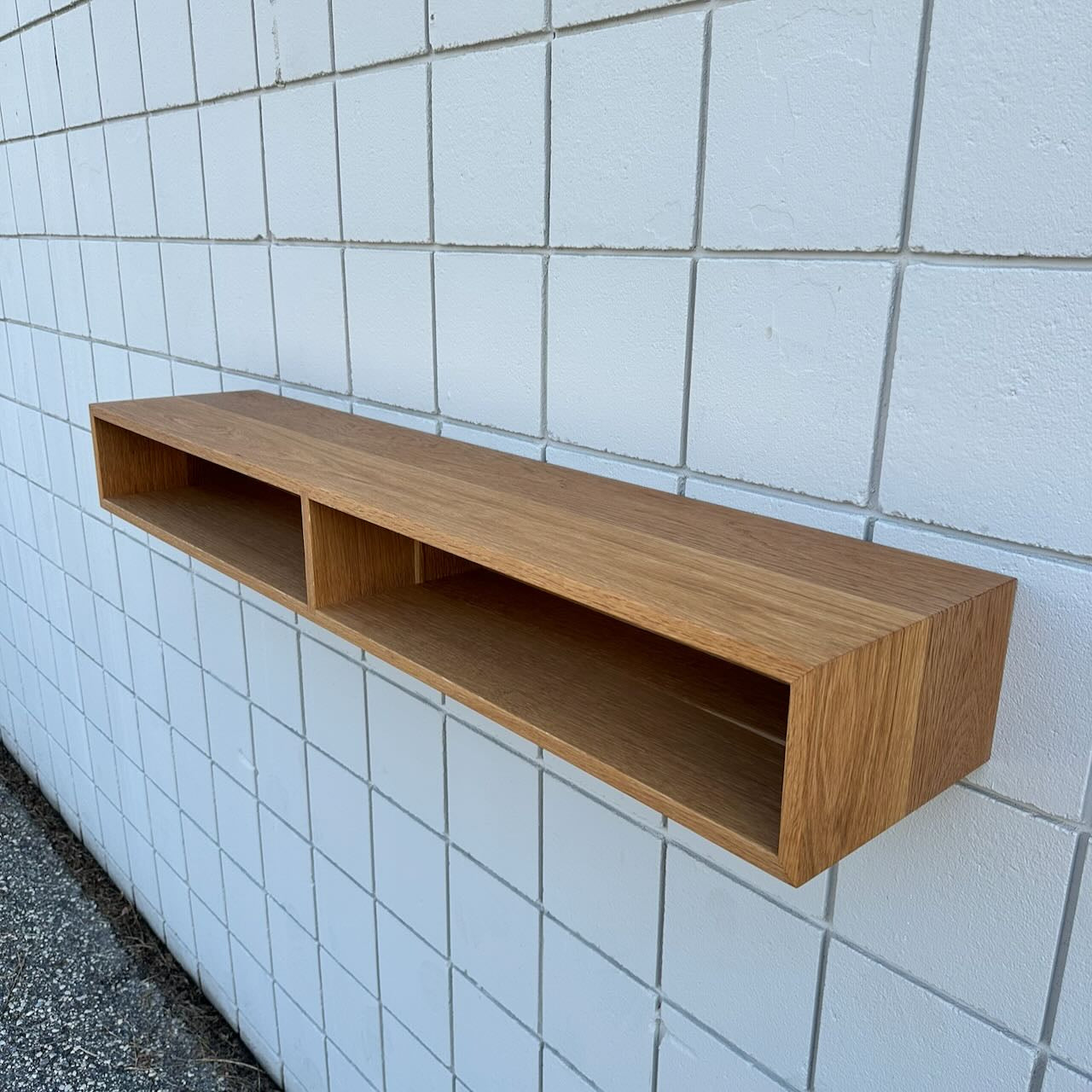 A modern Krovel Furniture Co. 48″ White Oak Console Table with two open compartments is mounted on a white tiled wall. Featuring clean, minimalist lines and a natural white oak finish, this console is an ideal VOC-free furniture choice for your space.