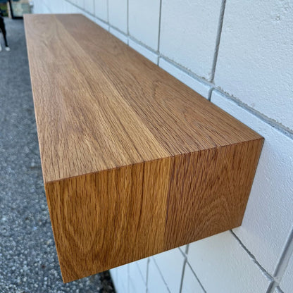 A close-up of Krovel Furniture Co.’s 48″ White Oak Console Table - SAMPLE, its smooth finish and visible wood grain standing out as it floats against a white tiled wall. The gravelly ground below adds texture, while a blurred dog’s legs appear in the top left corner.