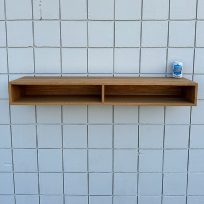 A 48″ White Oak Console Table by Krovel Furniture Co. is mounted against a white tiled wall, its two open compartments reflecting clean, modern lines. On the top right corner of this VOC-free furniture piece, a can of La Croix sparkling water is placed.