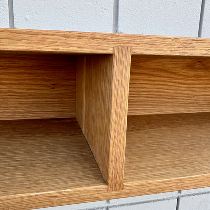 A close-up view of the 48″ White Oak Console Table by Krovel Furniture Co. highlights its vertical divider and the distinctive natural wood grain of this VOC-free piece. In the background, a white tiled wall with visible grout lines enhances the display.