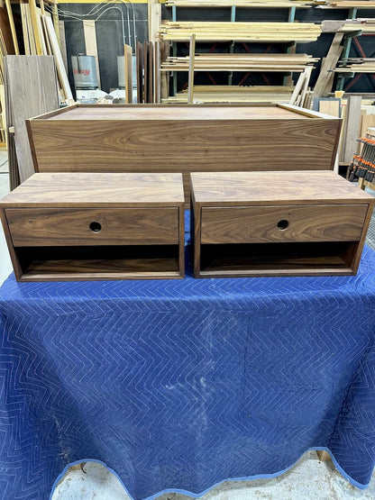 Two small walnut floating nightstands from Krovel Furniture Co. (PAIR (2) Walnut Floating Nightstands - SAMPLES) and one larger cabinet are displayed on a blue fabric in a workshop with wood panels and tools in the background.