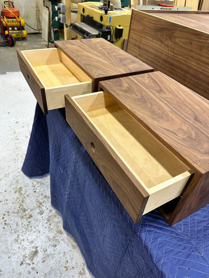 A pair of wooden drawers with dovetail joints, crafted from solid Hard Maple and partially pulled out from a matching cabinet, are displayed on a blue padded cover in a workshop setting. These drawers are featured as samples for the PAIR (2) Walnut Floating Nightstands by Krovel Furniture Co. and come with a durable, VOC-free finish.