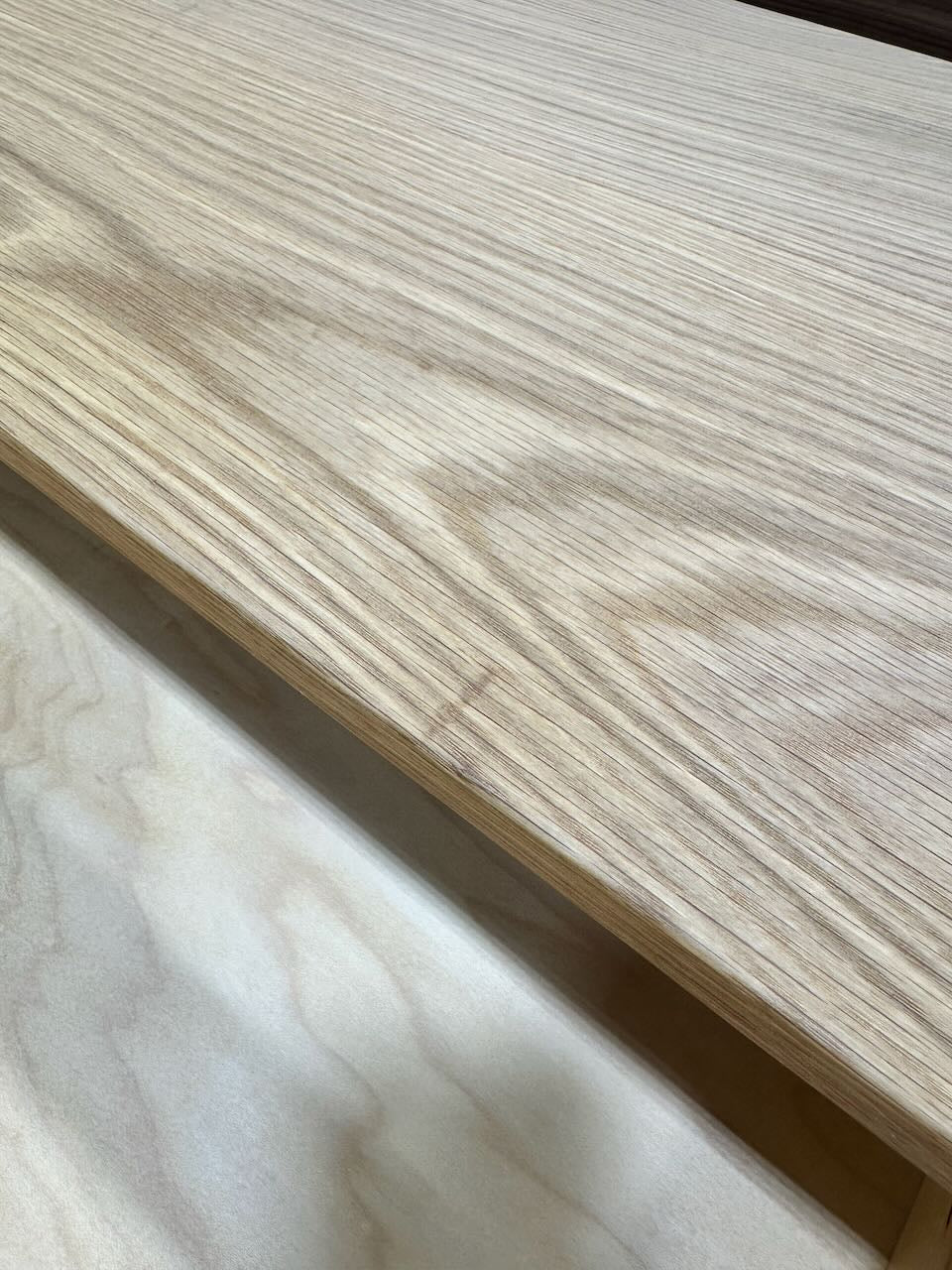 A pair of wooden boards is stacked, showcasing contrasting grain patterns. The top board—crafted from solid White Oak by Krovel Furniture Co.—displays a striking, wavy wood grain, while the bottom board features a lighter tone with a smoother and more understated texture. These elegant details exemplify the craftsmanship found in PAIR (2) White Oak Floating Nightstands - SECONDS by Krovel Furniture Co.