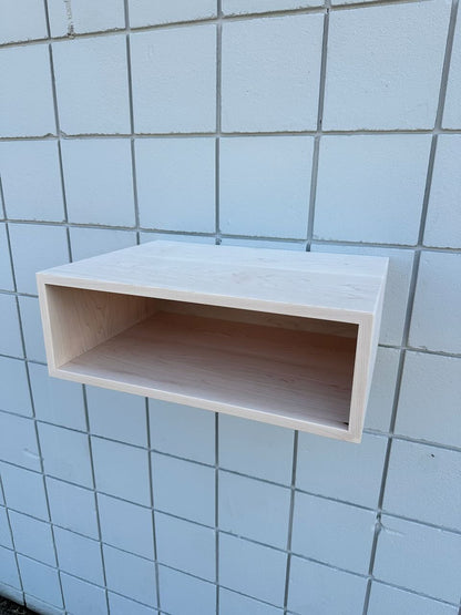 A light natural wood floating wall shelf mounted on a white tiled wall.