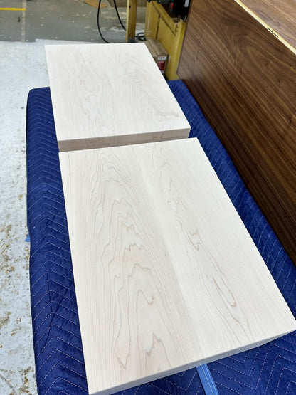 Tops of two light wood storage shelves with visible grain patterns resting on a blue quilted moving blanket in a workshop setting.