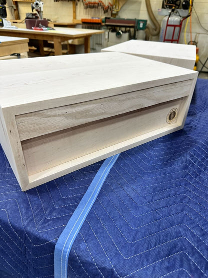 Rear view of wooden nightstand with a recessed panel, resting on a blue quilted moving blanket in a workshop setting.