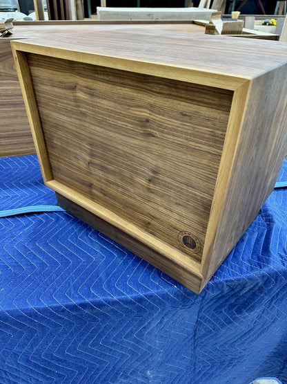 Back of wooden nightstand with a rich walnut-grain finish, resting on a blue moving blanket in what appears to be a workshop or warehouse setting.