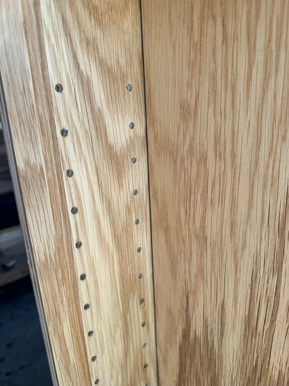 Close-up of a light oak wood cabinet door showing the wood grain texture and a row of pre-drilled screw holes along the edge.
