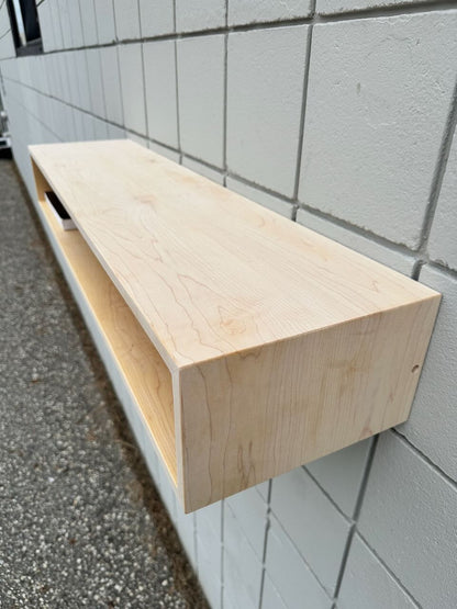 A Maple Console Table - UNFINISHED by Krovel Furniture Co. is mounted on a white tiled wall outdoors above a gravel surface, showcasing the simple elegance characteristic of discounted furniture.