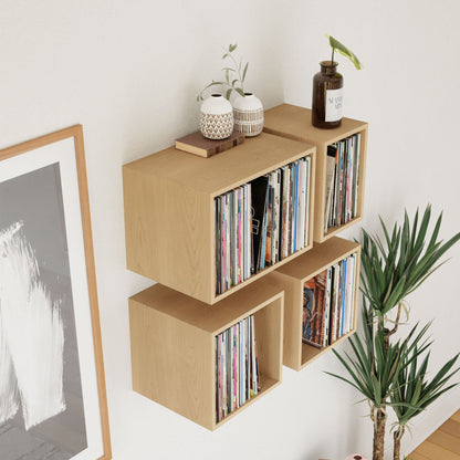 Four Krovel Record Storage Shelves in Maple display vinyl records, accented with ceramic vases, a candle, and a glass bottle plant. Nearby, a green potted plant and abstract art complete the charming setup.