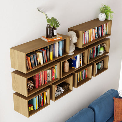 The Krovel Floating Bookshelf in White Oak displays books, a small plant, a bust sculpture, and decorative accents, all stylishly arranged above a blue sofa.