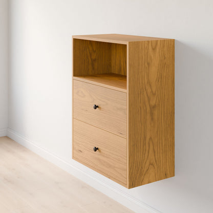 The Krovel Furniture Co. Maine Made Closet Drawers is a wooden wall-mounted cabinet with an open upper shelf and two drawers featuring small round black knobs, shown fixed to a white wall above a light wood floor.