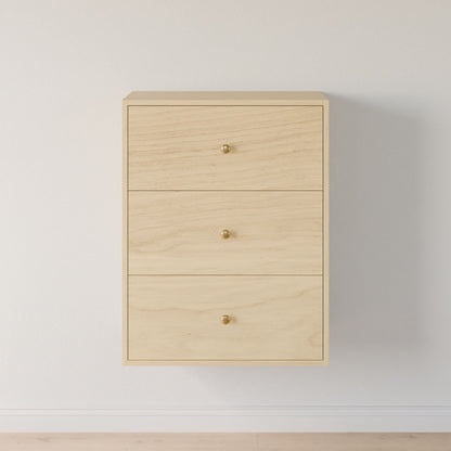 The Maine Made Closet Drawers by Krovel Furniture Co. is a minimalist light wood cabinet with three drawers and round gold knobs, mounted on a white wall above a light floor. Crafted from premium cabinet plywood.