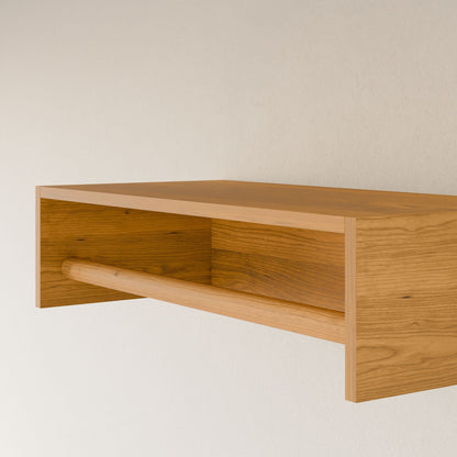 The Closet Hanger in Cherry by Krovel Furniture Co. is a wall-mounted wooden shelf handcrafted in Portland, Maine. Made from premium grade plywood, it has a natural finish that highlights its wood grain against a white wall and features an open-front design with a horizontal support bar forming a trapezoidal space.