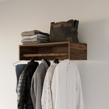 The Maine Made Closet Hanger by Krovel Furniture Co. is a wooden, wall-mounted shelf that neatly displays sweaters and a bag on top, with jackets and shirts hanging below, handmade in Portland, Maine against a plain white wall.