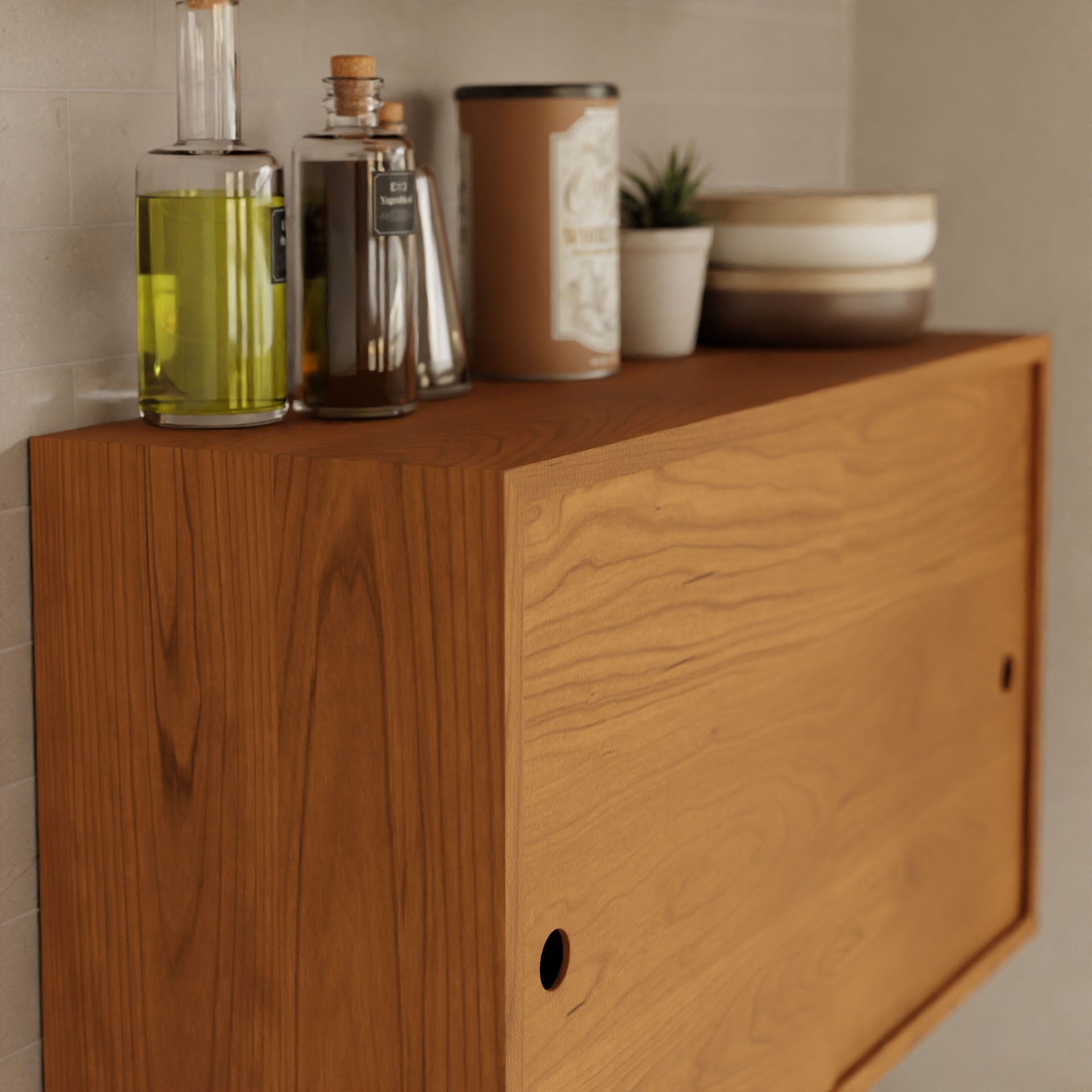 The Krovel Cupboard with Shelf in Cherry elegantly holds bottles of oil and vinegar, a tin can, a potted plant, and stacked bowls. Its minimalist design complements the tiled background, giving it the appearance of a floating storage cabinet.