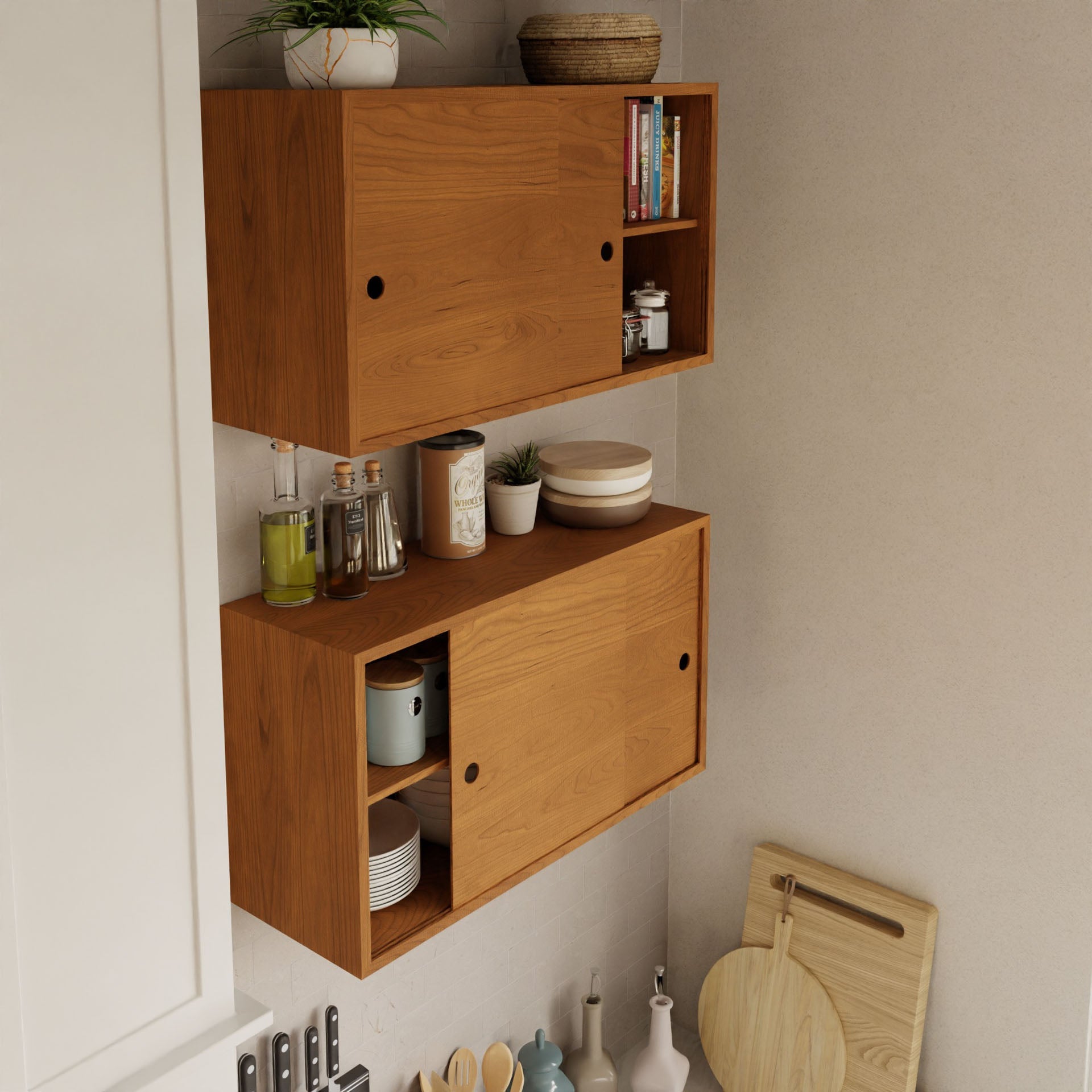 The Krovel Cupboard with Shelf in Cherry elegantly displays plates, pots, and books on sliding shelves. Potted plants adorn one shelf, while the countertop below holds oil bottles. Cutting boards, knives, and jars are neatly arranged against a light wall in this stylish floating storage cabinet setup.