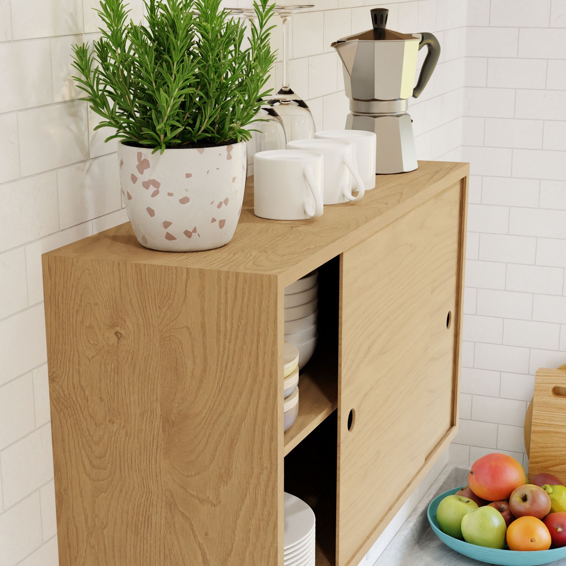 A Krovel Cupboard with Shelf in Maple features sliding doors storing white dishes and mugs. It is topped with a potted plant, metal stovetop espresso maker, three white mugs, and complemented by a nearby bowl of assorted fruits for an elegant touch.