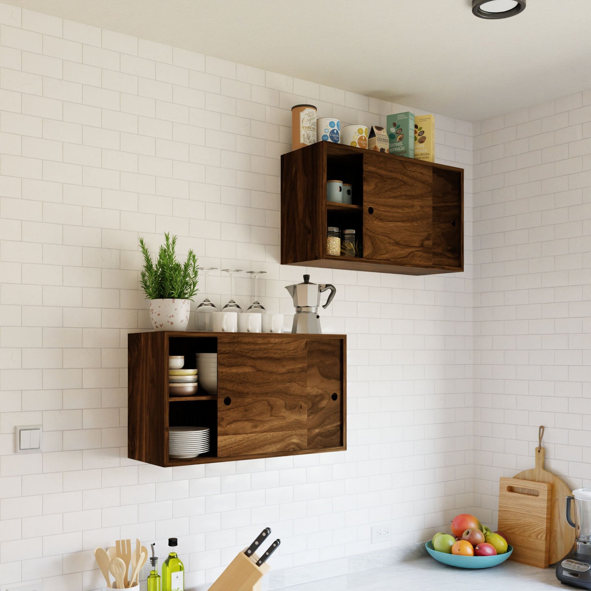 A minimalist kitchen with white subway tiles showcases a Krovel Cupboard with Shelf in Walnut. The lower shelf holds kitchen items and a plant, the upper stores canned goods, while the counter below displays cutting boards, a knife, and a bowl of fruit.