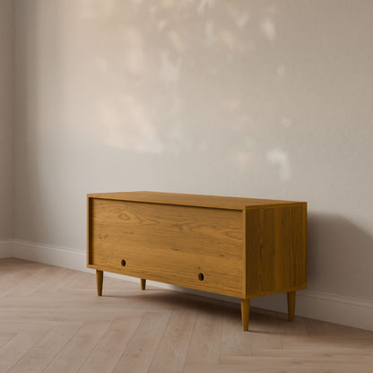 The Krovel Furniture Co. Double Door Media Cabinet in Cherry features a sleek, modern design with tapered legs crafted from formaldehyde-free hardwood veneer. When placed against a light-colored wall, sunlight creates soft shadows and leaf patterns on the floor for a warm, inviting atmosphere.