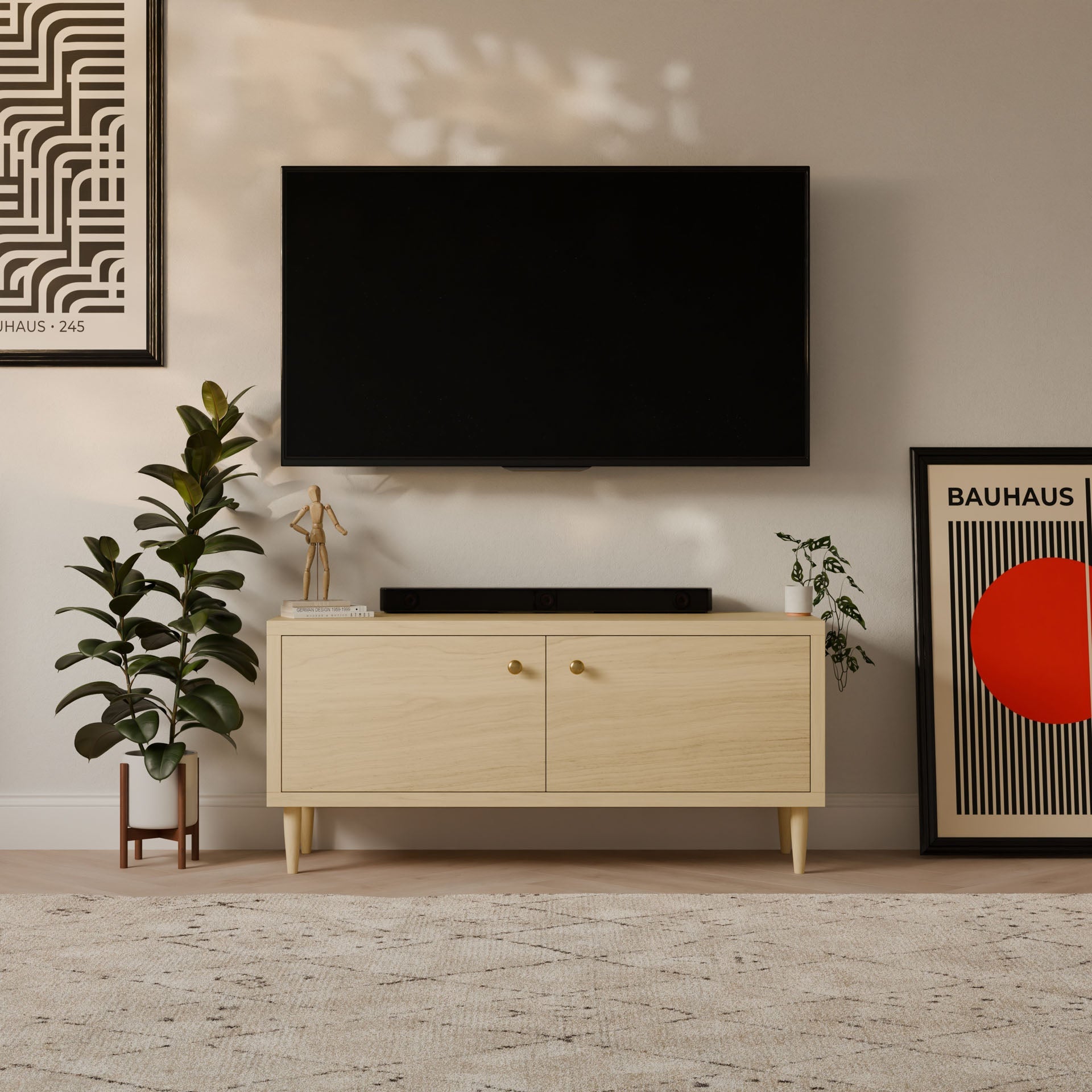 A contemporary living room showcases a wall-mounted flat-screen TV above Krovel Furniture Co.s customizable Double Door Media Cabinet in Maple, crafted in Portland, Maine, from formaldehyde-free hardwood. The decor is finished with two plants, a sculpture, and abstract art on a light rug.