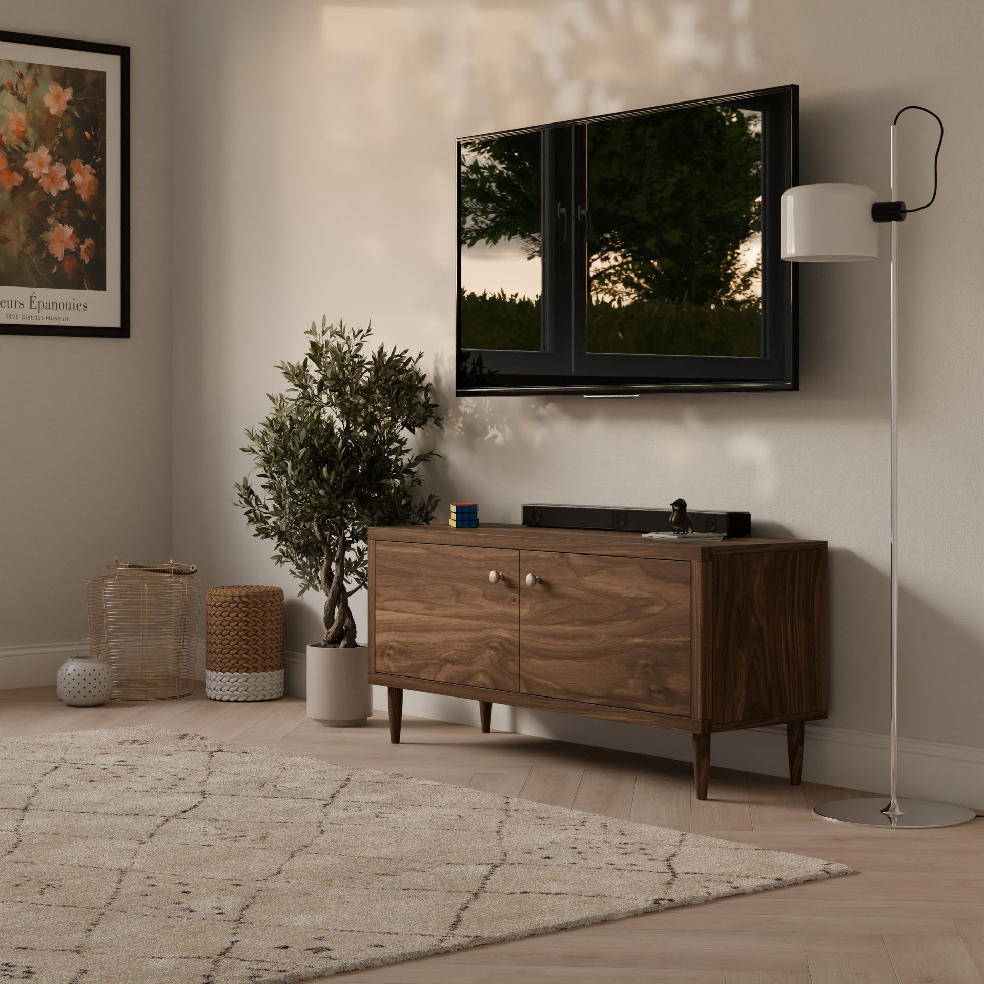 In a cozy living room corner, a wall-mounted TV sits above Krovel Furniture Co.s Double Door Media Cabinet in Walnut. A tall potted plant and floor lamp add charm, natural light filters through the window, and a decorative rug covers the floor beneath framed flower artwork.