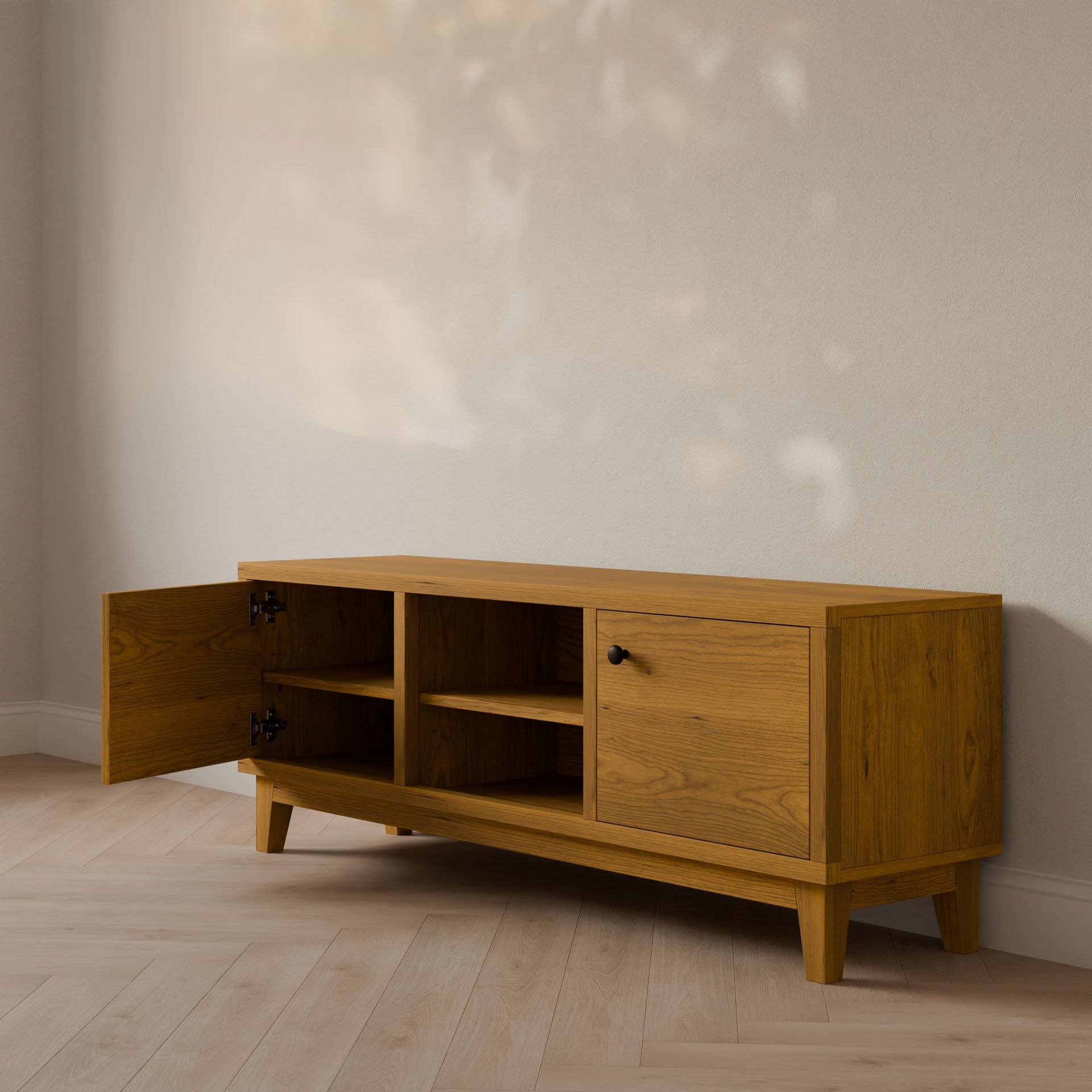 Handcrafted in Portland by Krovel Furniture Co., this wooden Double Door, Open Shelf Media Cabinet in Cherry features a sleek design with tapered legs. Its left door is ajar, showcasing shelves made from formaldehyde-free hardwood veneer, while leafy shadows dance on the light-colored wall behind it.