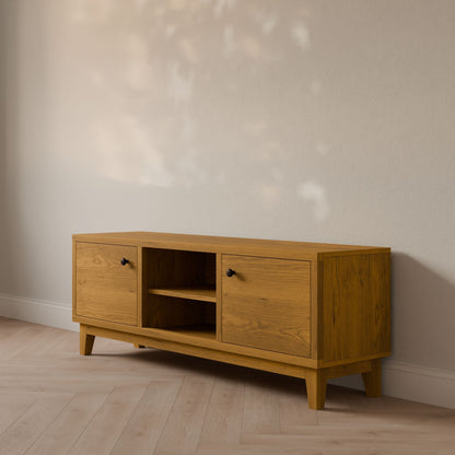 The Double Door, Open Shelf Media Cabinet in Cherry by Krovel Furniture Co. is a wooden sideboard with two cabinets and open shelving, set against a light wall. Soft lighting casts leaf-patterned shadows on its formaldehyde-free veneer as it rests elegantly on a light hardwood floor.