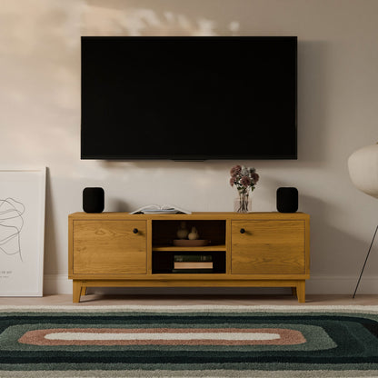 A flat-screen TV is mounted above a Krovel Furniture Co. Maine Made Double Door, Open Shelf Media Cabinet with books, vases, and black speakers. A framed abstract art piece, a lamp, and a patterned rug complete the scene.