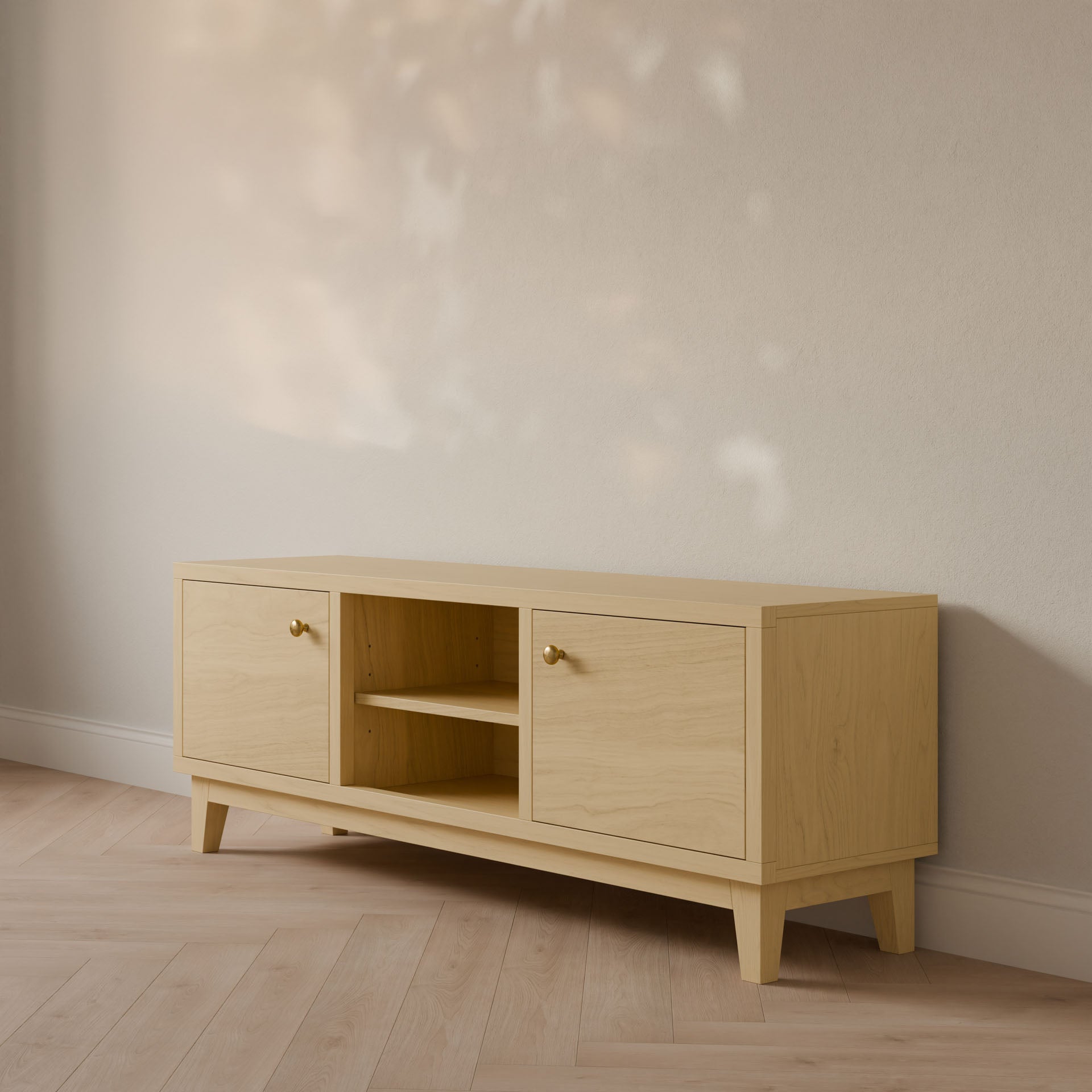 The Double Door, Open Shelf Media Cabinet in Maple by Krovel Furniture Co. rests against a cream wall, featuring two closed cabinets with round knobs and a central open shelf. Its customizable design complements the floor as soft light casts subtle shadows on the wall.