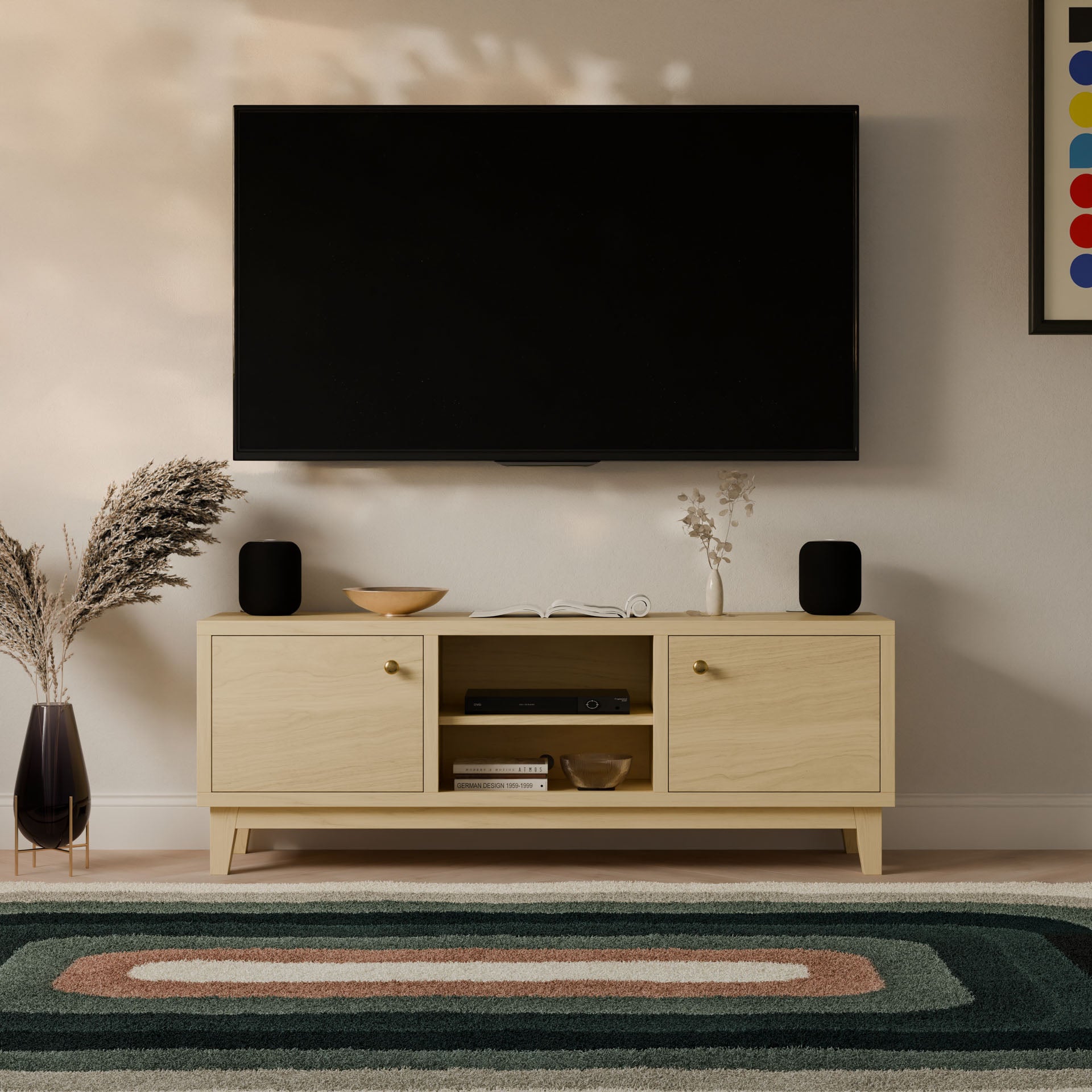 A modern living room setup includes a wall-mounted TV above the Krovel Furniture Co.s Double Door, Open Shelf Media Cabinet in Maple. This hardwood veneer cabinet holds electronics and decor. Speakers are on top, and an abstract-patterned decorative rug covers the floor.
