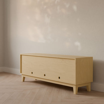 The Maine Made Double Door, Open Shelf Media Cabinet by Krovel Furniture Co. sits against a light wall on a parquet floor, featuring minimalist design and open shelves, bathed in soft natural light.