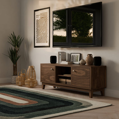 A modern living room features the sleek Double Door, Open Shelf Media Cabinet in Walnut by Krovel Furniture Co., with a TV mounted above. The cabinet stores books and decor, complemented by abstract art. A tall plant and woven baskets occupy the corner, and a geometric-patterned rug enhances the space.