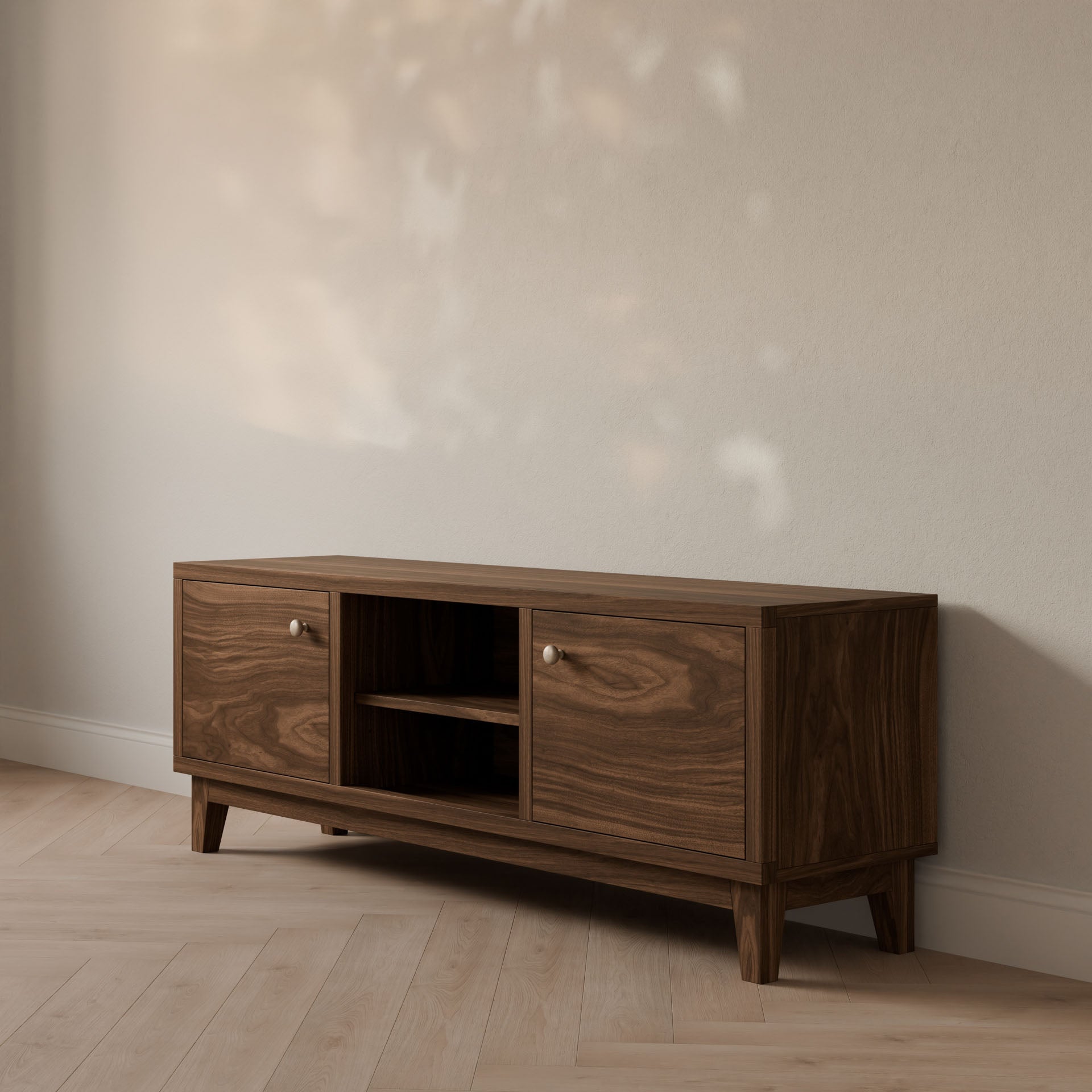 A Double Door, Open Shelf Media Cabinet in Walnut by Krovel Furniture Co. stands against a beige wall on a light wood floor, its hardwood veneer catching sunlight for a dappled effect.