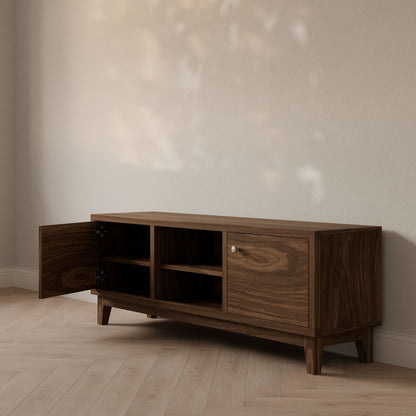 The Maine Made Double Door, Open Shelf Media Cabinet by Krovel Furniture Co. is a customizable, formaldehyde-free wooden sideboard with mid-century design, featuring one open left door and one closed right door on a light wood floor against a beige wall.