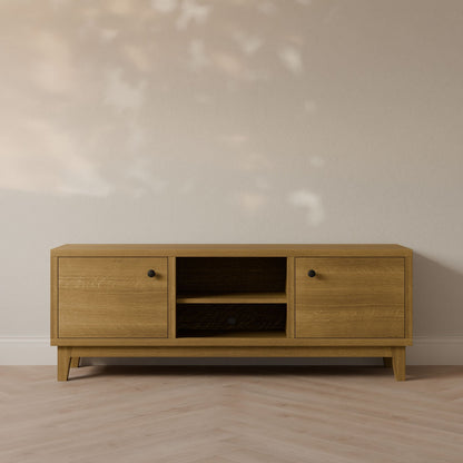 The Double Door, Open Shelf Media Cabinet in White Oak by Krovel Furniture Co. rests against a light wall, showcasing two cabinets with black knobs and central open shelving. Its minimalist design pairs beautifully with the floors subtle herringbone pattern and soft light casting gentle shadows.