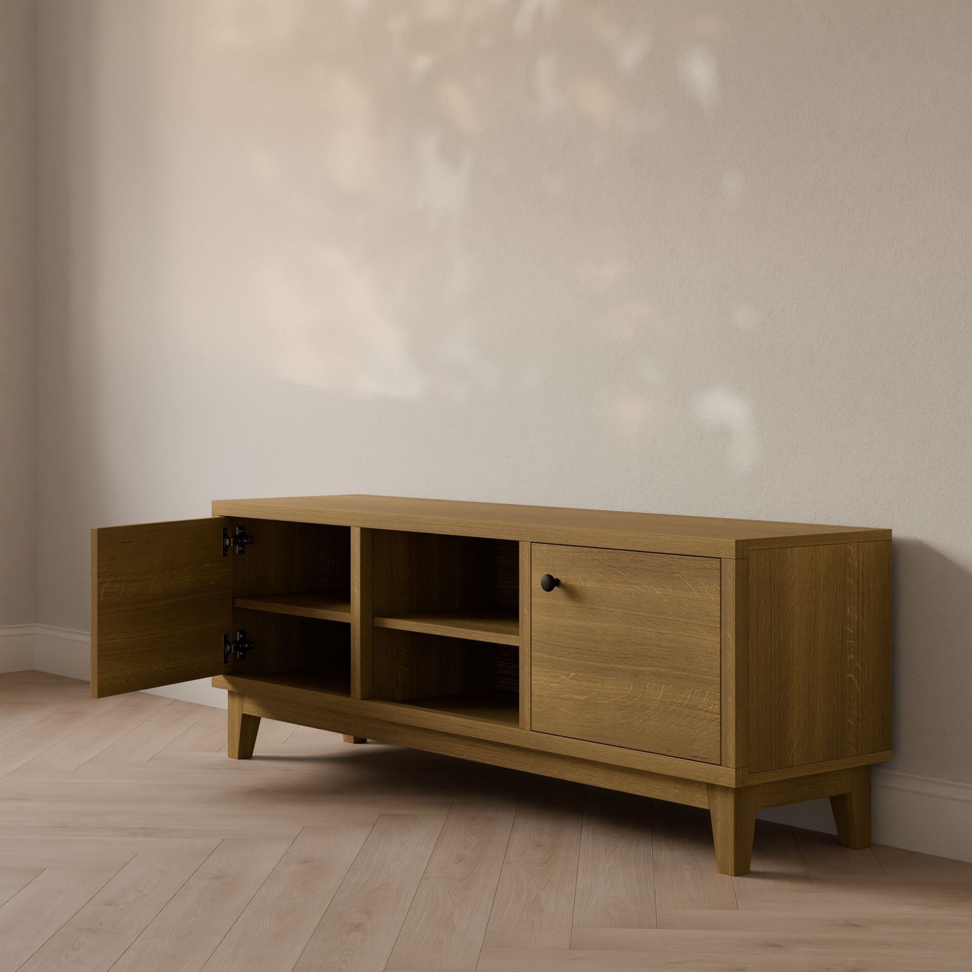 A Double Door, Open Shelf Media Cabinet in White Oak by Krovel Furniture Co. enhances the minimalistic room, its doors slightly ajar against a wooden floor. Soft light dances on the formaldehyde-free hardwood veneer surfaces, casting delicate shadows on the wall.