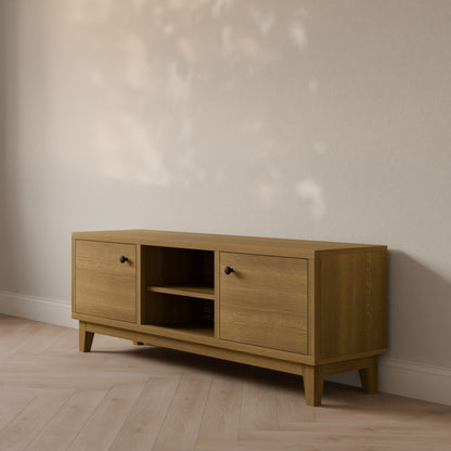The Double Door, Open Shelf Media Cabinet in White Oak by Krovel Furniture Co., handmade in Portland from formaldehyde-free hardwood veneer, rests against a wall. With two side cabinets and a central open shelf, it sits on a light-colored wood floor where dappled light casts gentle shadows.
