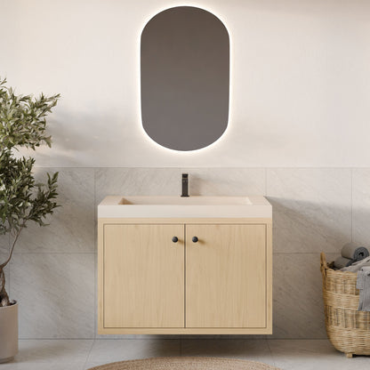 The Double Door Vanity in Maple by Krovel Furniture Co. features a light wood cabinet, white countertop, and black faucet beneath an oval backlit mirror. A towel basket and potted plant accent the tiled floor and wall nearby.
