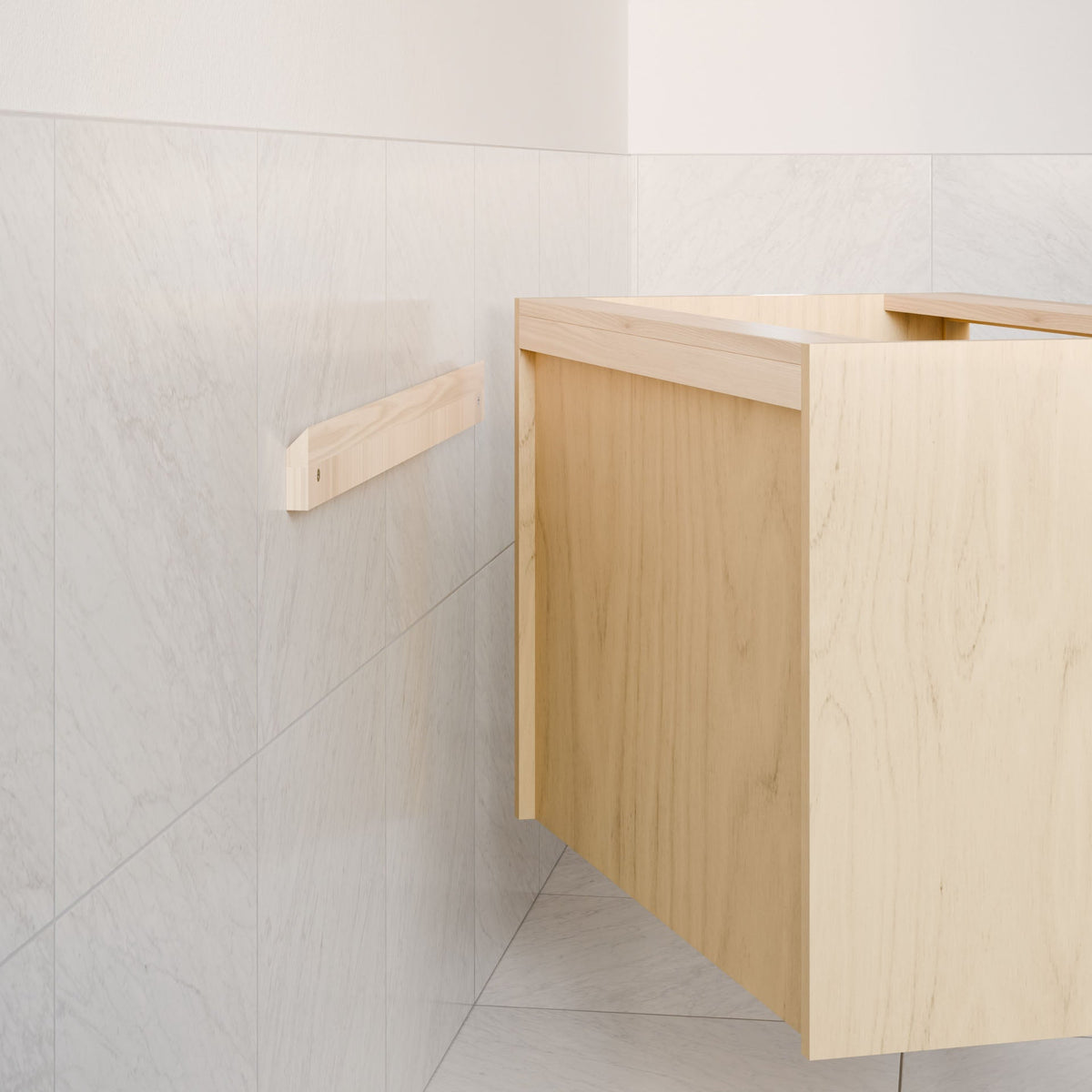 The Double Door Vanity in Maple by Krovel Furniture Co. is partially installed on a wall with light gray marble tiles, with a wooden support bracket mounted nearby.
