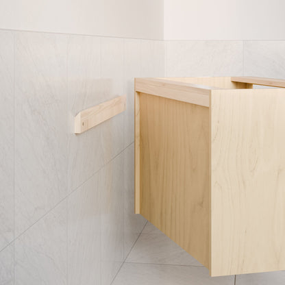 The Double Door Vanity in Maple by Krovel Furniture Co. is partially installed on a wall with light gray marble tiles, with a wooden support bracket mounted nearby.